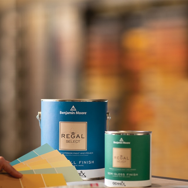 A blurred background focused on a large blue paint can next to a smaller green paint can featuring a color fan deck.
