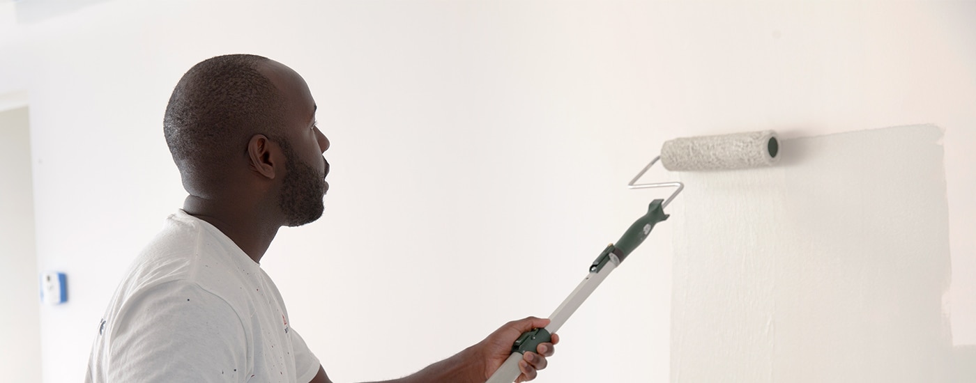 A painting contractor rolling white paint onto a primed wall.