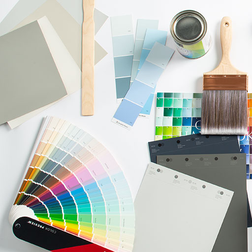 A desktop with paint swatches, paint, a brush and stir sticks amid a professional’s hard work.