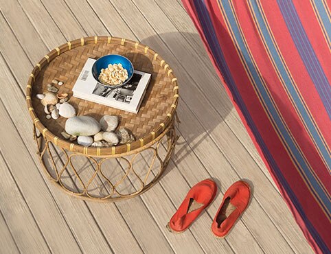 A light-stained wood deck with a round wicker table, red shoes, and a red and blue striped hammock.