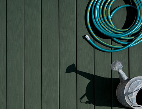 Hose and watering can on a green composite deck.