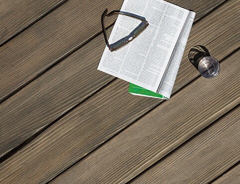 Magazine, lunettes de soleil et verre d’eau sur une terrasse en cèdre.