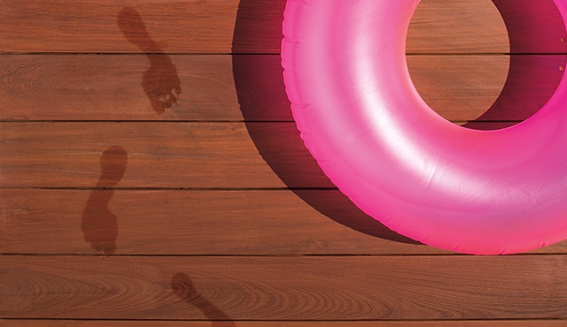 A stained deck with pink pool tube on it, and wet footprints. 