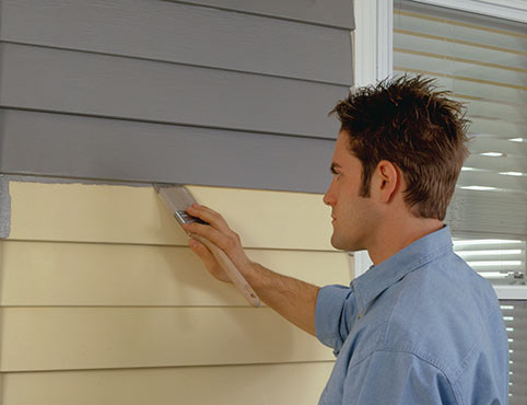 Man painting home exterior vinyl siding gray.