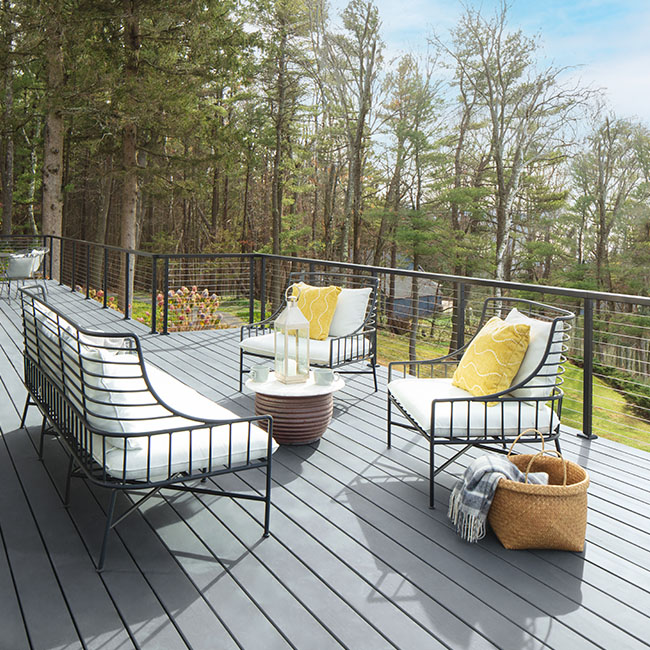 A set of black metal outdoor furniture with white cushions and yellow pillows on a spacious silvery blue stained deck.