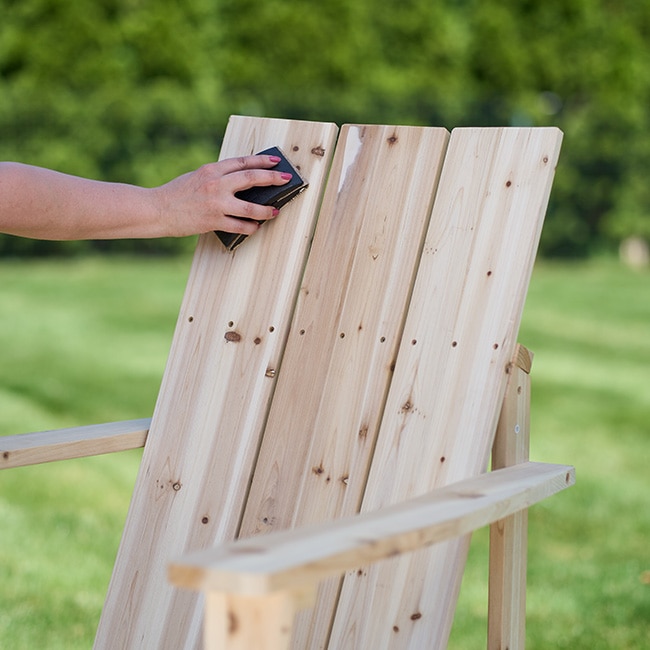 A closeup of someone sanding a wooden Adirondack chair.