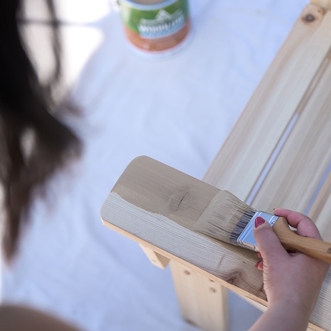 A closeup of someone applying exterior stain to a wooden chair.