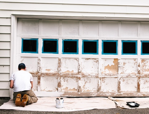 A person prepares to paint a garage door in a few simple steps from prep to priming to painting.