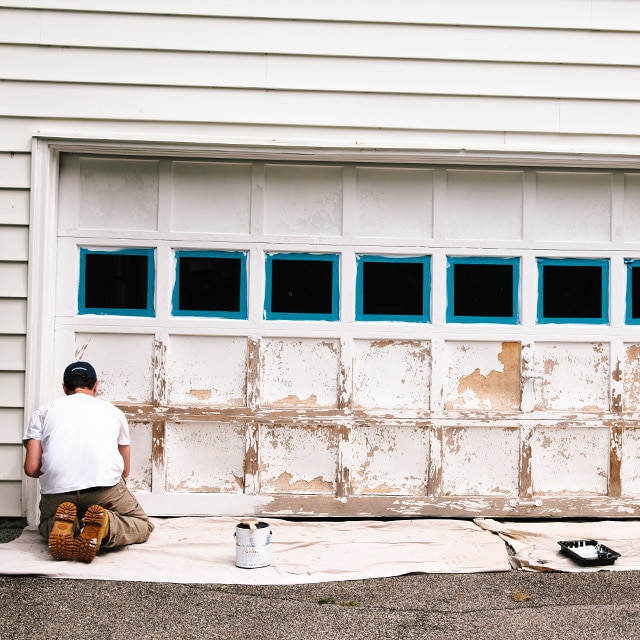 A person prepares to paint a garage door in a few simple steps from prep to priming to painting.