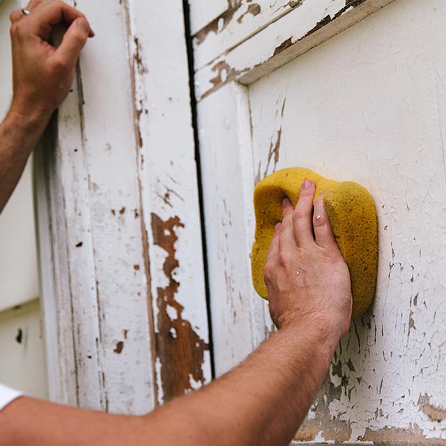 A person preps a garage door for painting by cleaning it first.