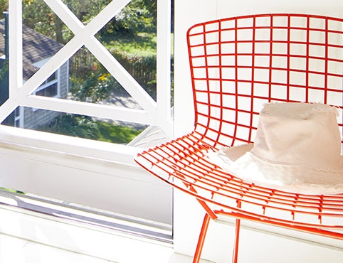 A bright red painted metal chair with a hat on it in an entryway beside an open door painted in charcoal gray.