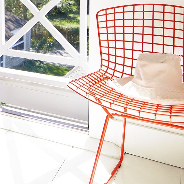 A bright red painted metal chair with a hat on it in an entryway beside an open door painted in charcoal gray.