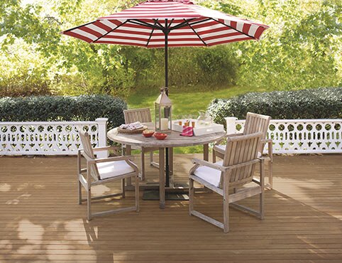 Outdoor wooden deck with matching table and chairs with a red stripped umbrella.