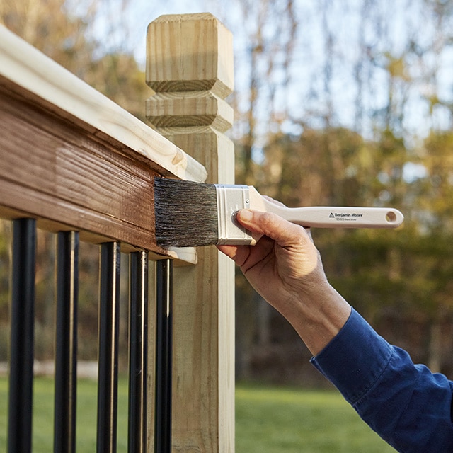 Una persona aplica tinte con brocha en la barandilla de una terraza.