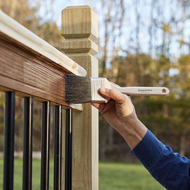 Une personne teint la balustrade d’une terrasse au pinceau.