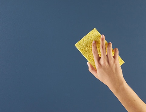 A person cleaning a blue painted surface with a sponge.