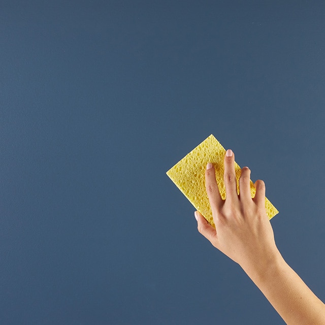 A person cleaning a blue painted surface with a sponge.