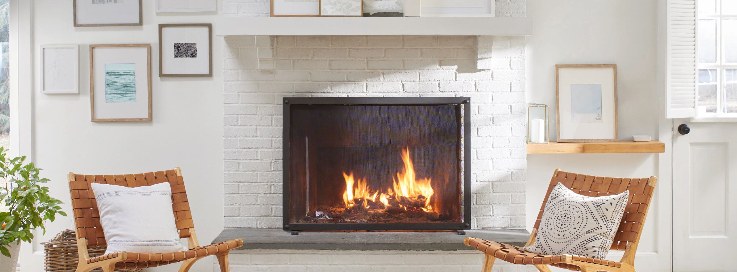 A white wall with framed artwork and white-painted brick fireplace flanked by matching leather and wood chairs.