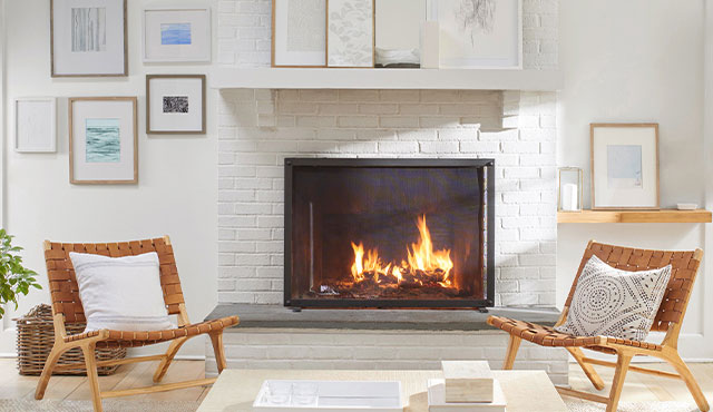 Un mur blanc arborant des œuvres encadrées et une cheminée en briques blanches entourée de fauteuils assortis en bois et en cuir.