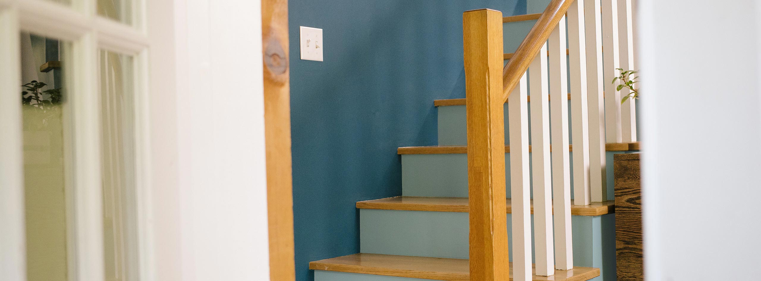 Escalier avec mur bleu, contremarches bleu pâle, balustres blancs et plans de marche et rampes en bois naturel.