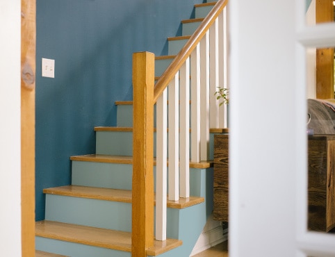 Escalier avec mur bleu, contremarches bleu pâle, balustres blancs et plans de marche et rampes en bois naturel.