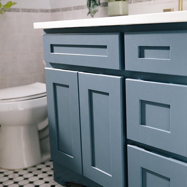 A blue painted bathroom vanity with white countertops.