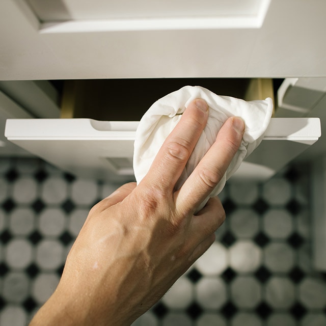 Cleaning the bathroom vanity with a damp cloth.