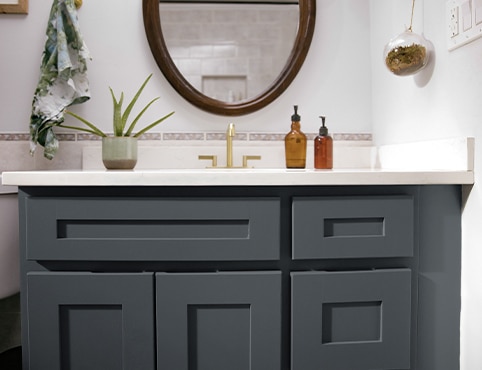 A close-up of a dark bathroom vanity cabinet, white countertops, muted pink tile backsplash, and one indoor plant.