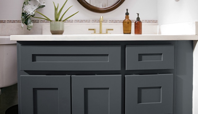 A close-up of a dark bathroom vanity cabinet, white countertops, muted pink tiles backsplash, and one indoor plant.