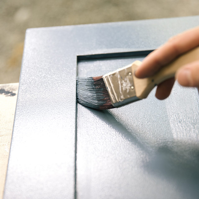 A homeowner painting bathroom cabinets using a paintbrush and ADVANCE Interior Paint.