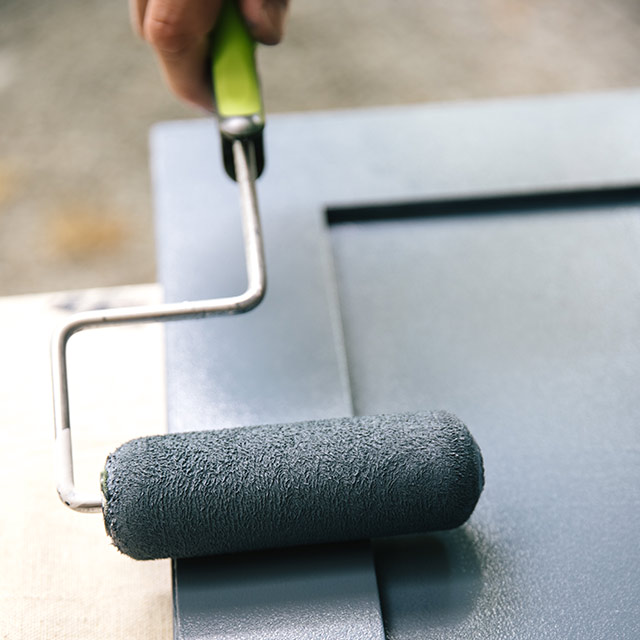 A homeowner painting bathroom cabinets blue using a roller and Benjamin Moore ADVANCE® Interior Paint.