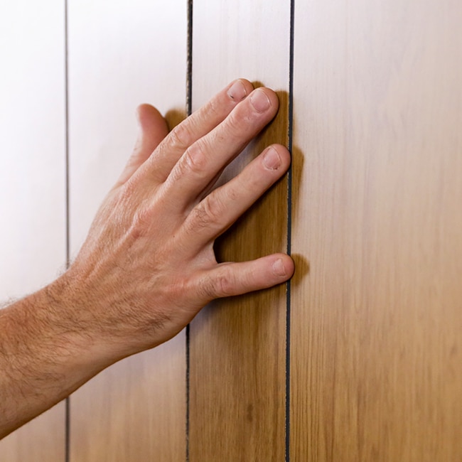 A homeowner touches wood paneling to determine the type.