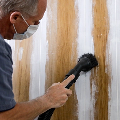 A homeowner wearing a dust mask sands the caulked grooves of wood panelling.