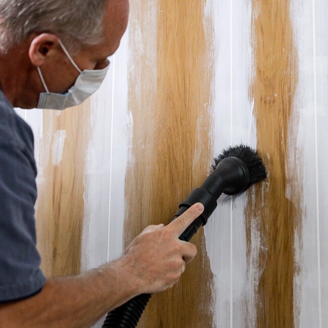 A homeowner wearing a dust mask sands the caulked grooves of wood panelling.