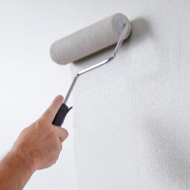 Un bricoleur finit de recouvrir de peinture blanche le mur lambrissé au rouleau.