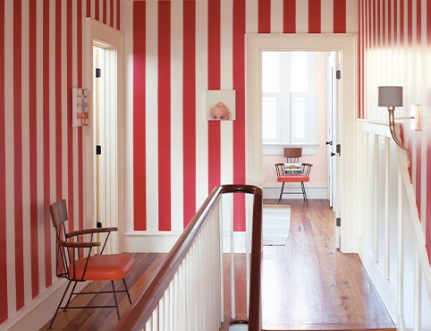 Hallway with red- and white-stripe painted walls, midcentury chair, funky wall art, white trim and wainscotting, and stairs.