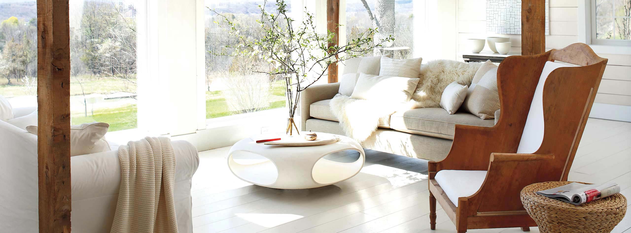 A living room with white-painted walls and floor, a wooden armchair, cozy sofas, and a modern coffee table.