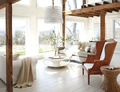 Un salon présentant des murs et un plancher peints en blanc, un fauteuil en bois, des canapés confortables et une table basse moderne.