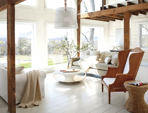 A living room with white-painted walls and floor, a wooden armchair, cozy sofas, and a modern coffee table.