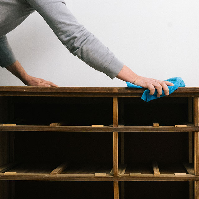 Cleaning surface of a dresser cabinet with a wet rag.