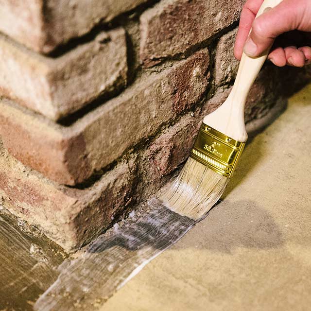 A homeowner applies sealer to a floor using a paintbrush.