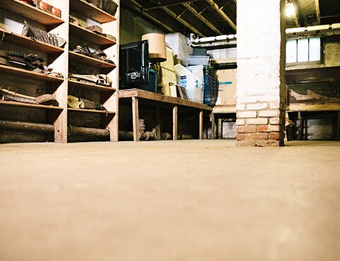 Un plancher de garage en béton qui a besoin d’être scellé. Une colonne en brique se trouve au milieu de la pièce, et des étagères en bois bordent les murs.