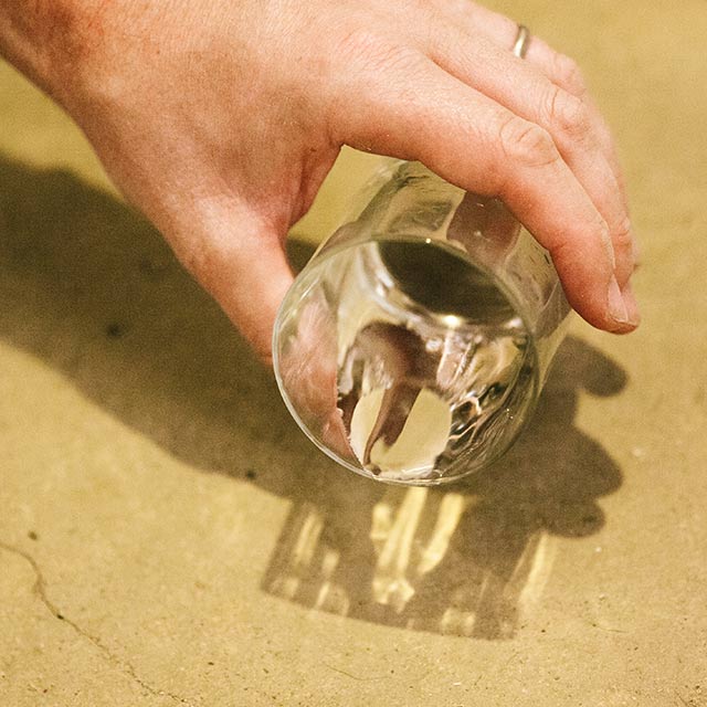 A homeowner tests a concrete floor by pouring a few drops of water from a small glass onto the floor.