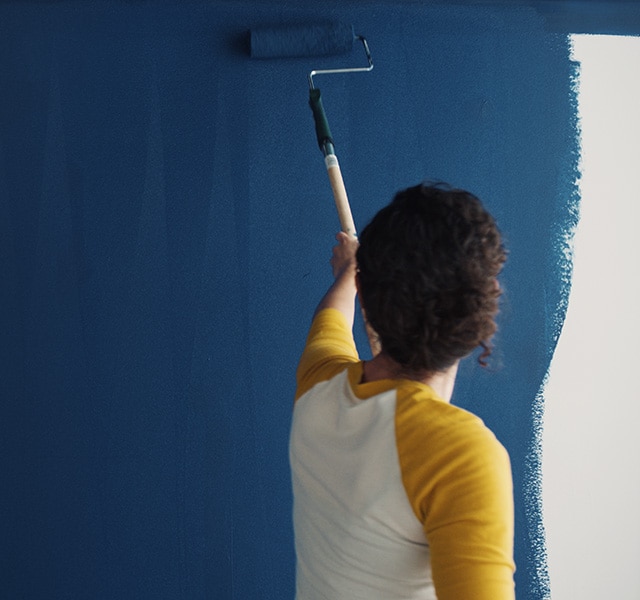 A homeowner uses a roller to paint Symphony Blue 2060-10 on a wall.