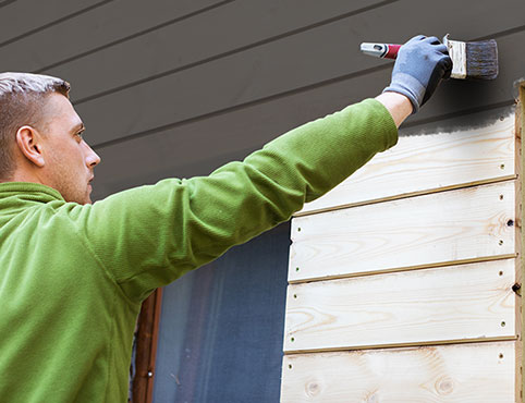 Un hombre pintando el exterior de una casa con un negro intenso.