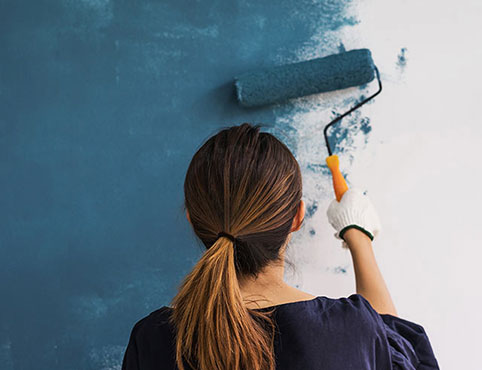 Femme appliquant au rouleau de la peinture bleue sur un mur.