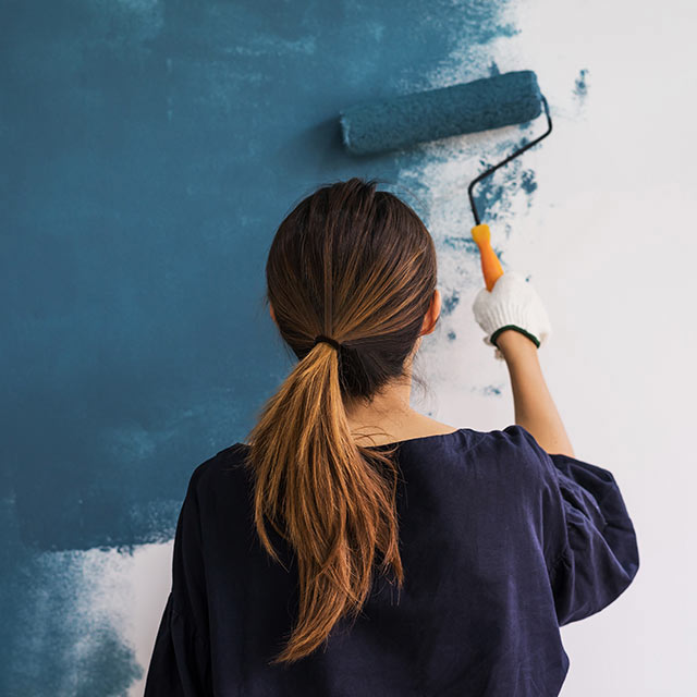 Mujer pintando una pared de azul con rodillo.