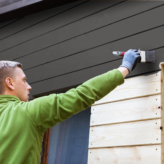 Un hombre pintando el exterior de una casa con un negro intenso.