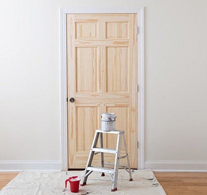 Step ladder, paint can, and tools sitting in front of a properly prepped door and wall.