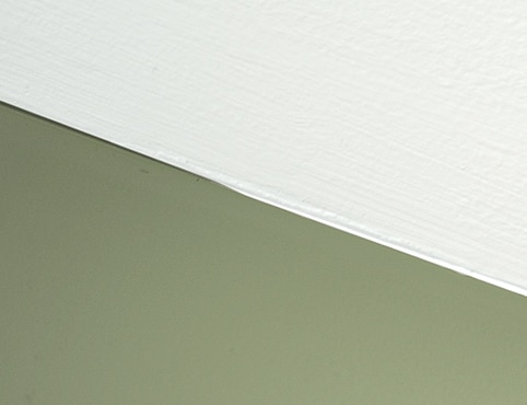 Close up of the seam between a white ceiling and a green wall.
